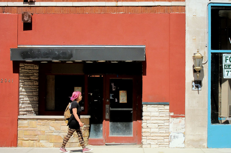 Pink haired woman with argyle leggings and pink sneakers walking past a long neglected storefront on a North Clark Street, Chicago